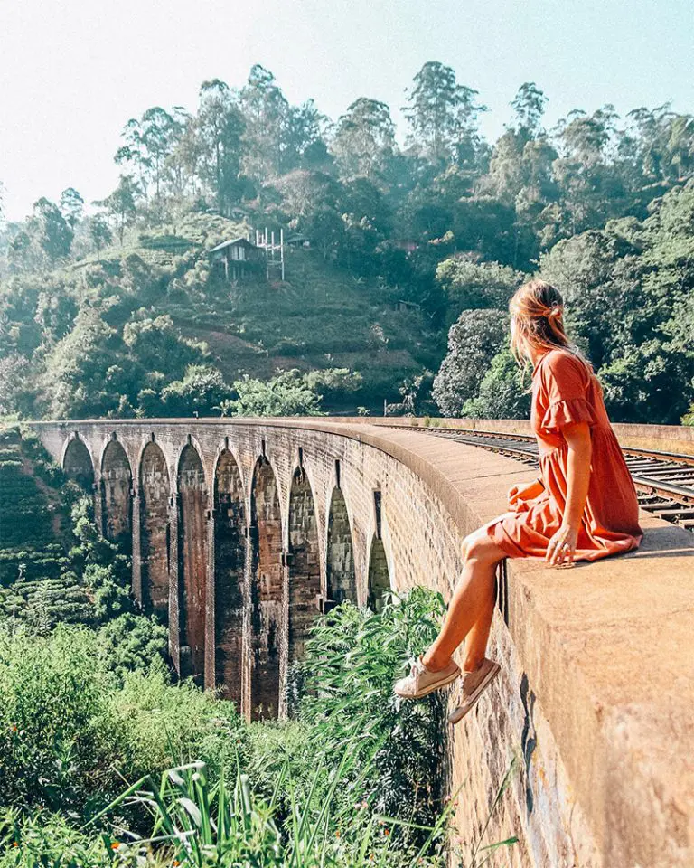 Traveler sitting on Nine Arches Bridge in Ella Sri Lanka surrounded by lush green hills and tea plantations